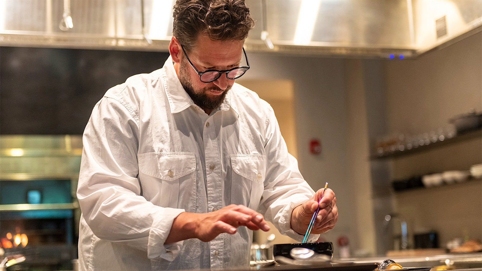  Chef Matthew Lightner, in a white shirt, prepare a dish in О̄kta's kitchen.
